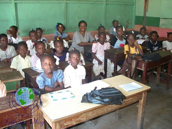 Students standing at their desks with two teachers in a Haiti classroom